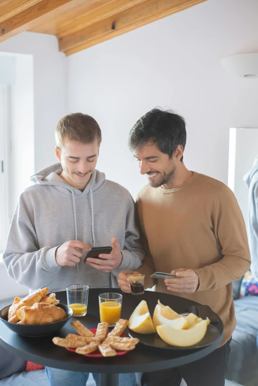 two men standing in front of a table with food on it, trending on reddit, happening, wearing pajamas, looking at his phone, home setting, thin young male