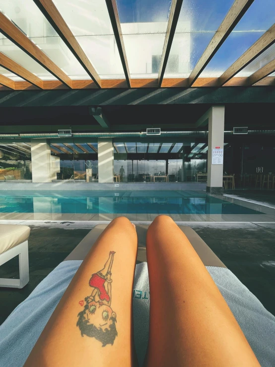 a person sitting next to a pool with a tattoo on their leg