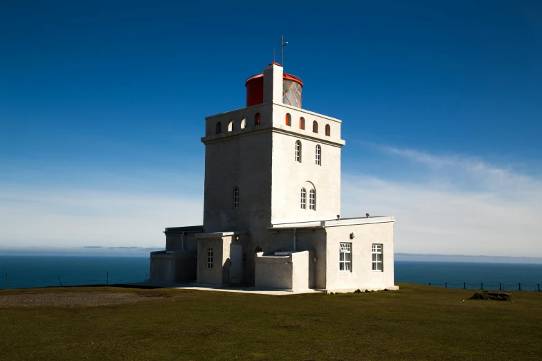 a white lighthouse sitting on top of a lush green hillside, by Hallsteinn Sigurðsson, square, exterior photo, blue sky, conde nast traveler photo