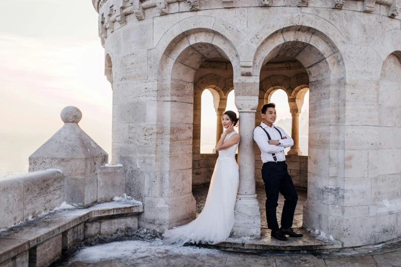 a man and a woman standing next to each other, by Emma Andijewska, pexels contest winner, art nouveau, bright white castle stones, tower, formal wear, sweeping arches