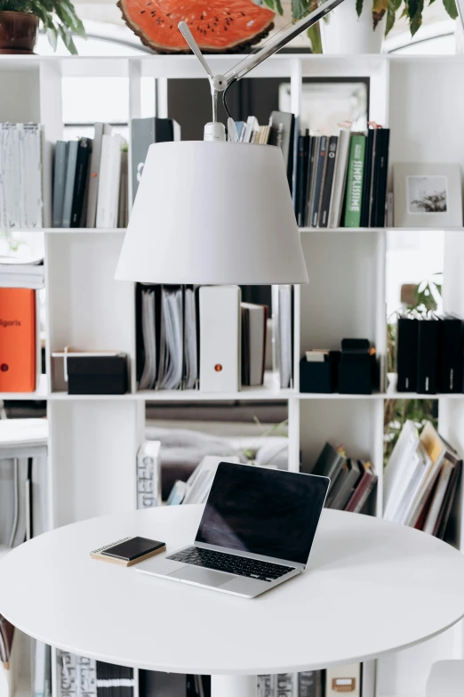 a laptop computer sitting on top of a white table, by Andries Stock, trending on unsplash, light and space, bookshelves on sides, famous designer lamp, scanning items with smartphone, dwell