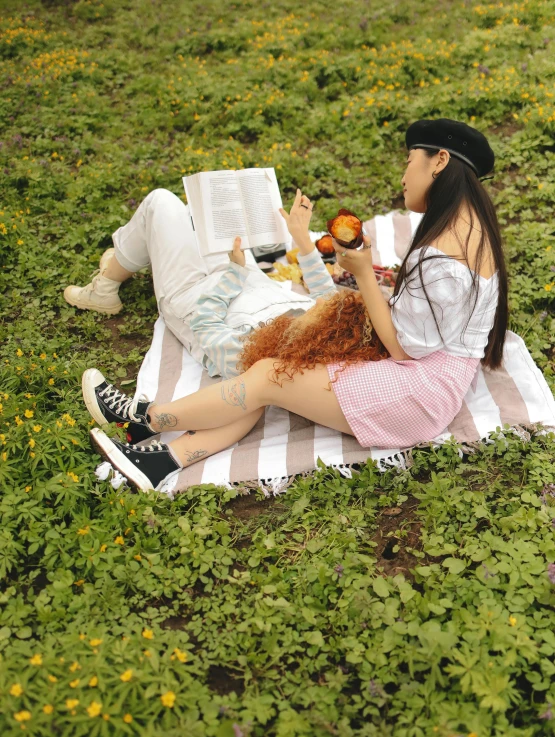 young woman laying on a field with grass, eating apples and reading
