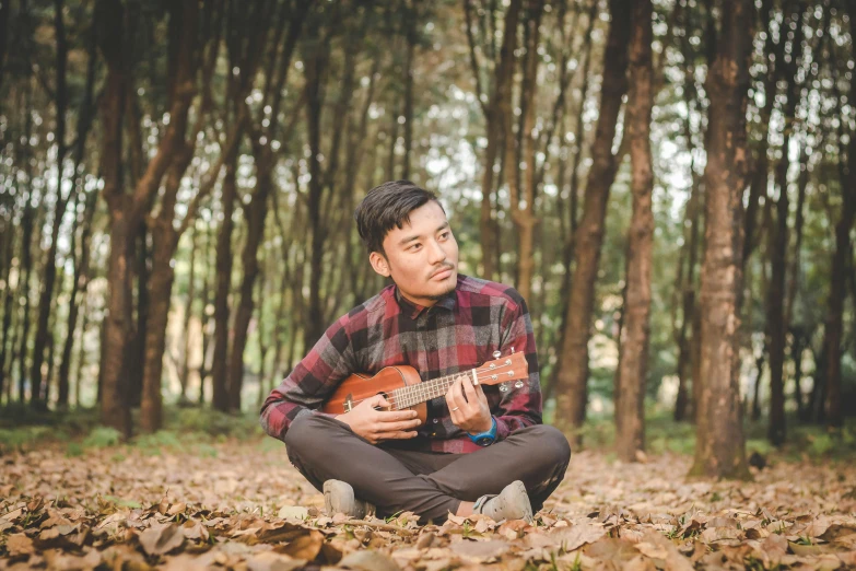 man sitting in the leaves playing a guitar