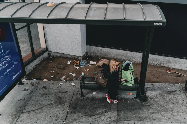 a woman sitting on a bench at a bus stop, pexels contest winner, cyberpunk homeless, belongings strewn about, san francisco, 2 people