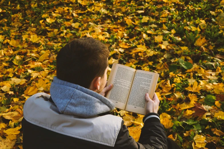 a man sitting on the ground reading a book, pexels contest winner, autumn colours, pictured from the shoulders up, avatar image, without text