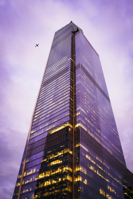 an airplane flying past a tall skyscr with purple clouds