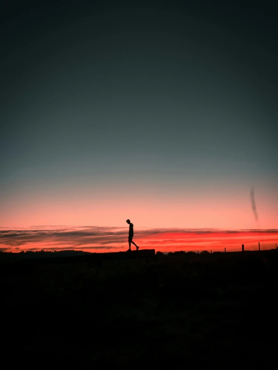 a person walking across a field at sunset, pexels contest winner, gradient red to black, carson ellis, profile picture, skies