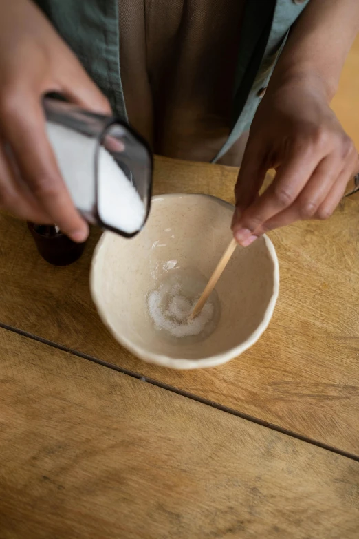 a person stirring something in a bowl on a wooden table, toothpaste refinery, square, medium, salt