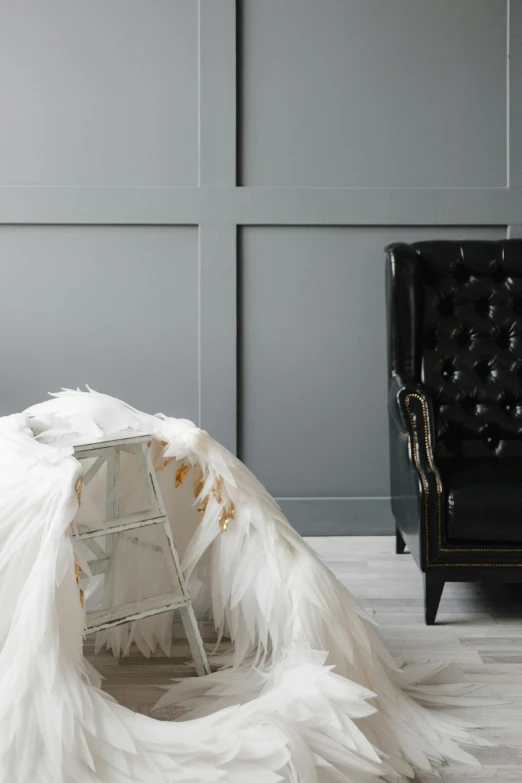 a woman in a wedding dress sitting on a chair, inspired by Cecil Beaton, trending on unsplash, leather sofa, with real wings, white bed, angle view