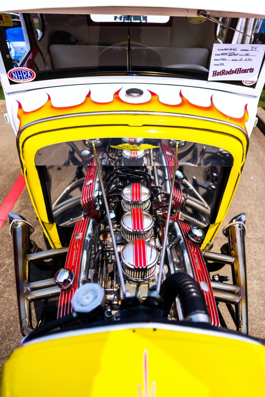 a close up of a yellow car with flames on the hood, inspired by Ed Roth, ford model t, symmetrical details, red and yellow scheme, with big chrome tubes