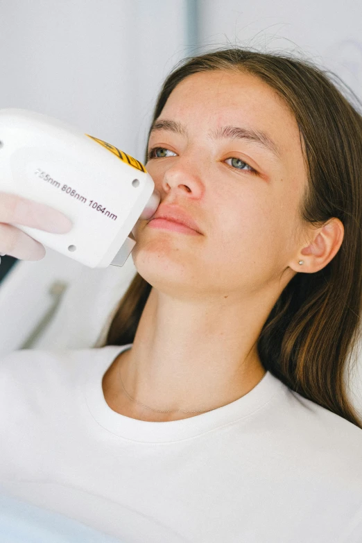 a woman is using a hair dryer on her face, by Adam Marczyński, unsplash, aestheticism, square facial structure, white and yellow scheme, medical image, laser