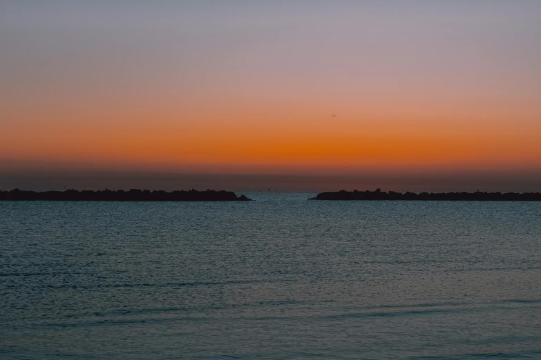 the sun is setting over a body of water, a picture, unsplash, romanticism, red sea, shot on sony a 7 iii, shot on 1 5 0 mm, city lights on the horizon