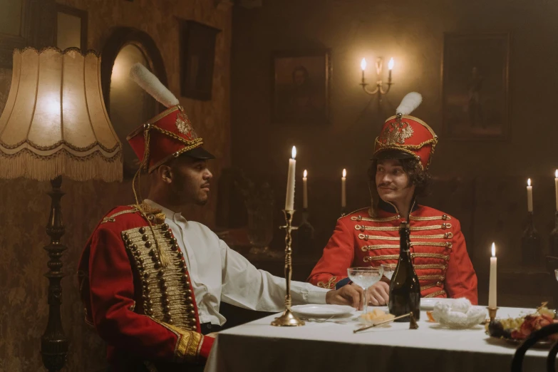 two men sitting at a table wearing costumes with plates of food