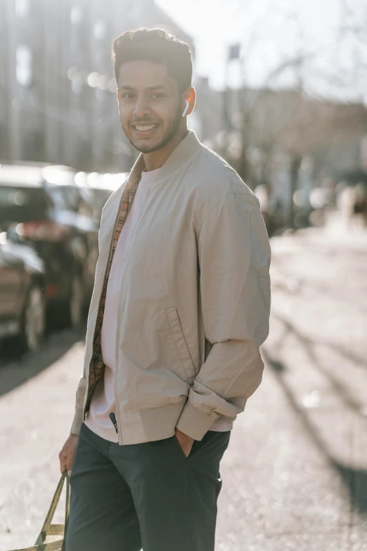 a man standing on the side of a road holding a bag, inspired by Harrington Mann, trending on pexels, renaissance, wearing a bomber jacket, light grey, khakis, smiling slightly