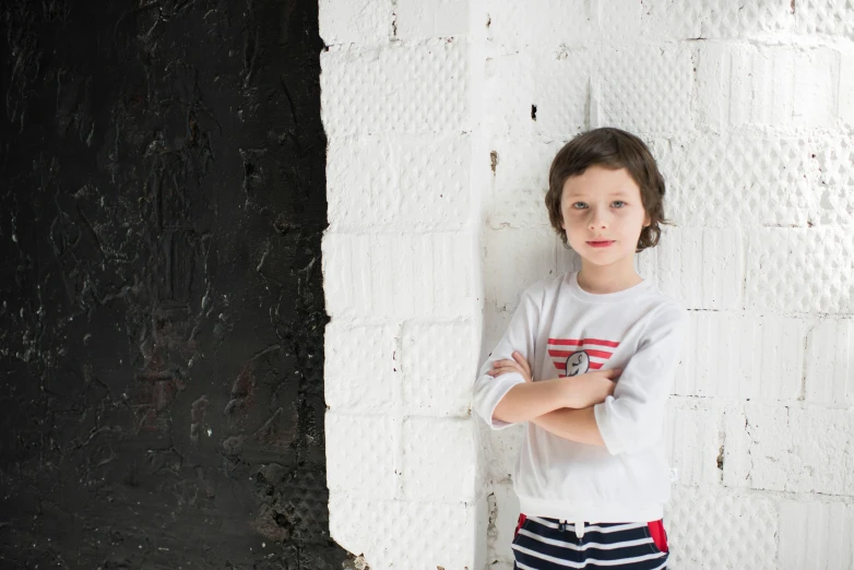 a young boy leaning against a wall with his arms crossed, an album cover, inspired by Thomas Struth, pexels contest winner, white wall, miro petrov, 15081959 21121991 01012000 4k, dezeen