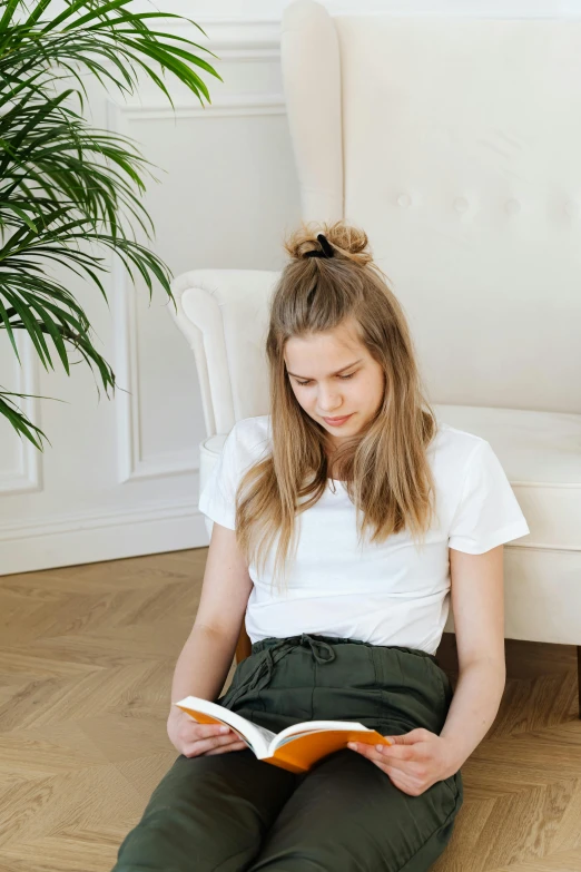 a woman sitting on the floor reading a book, by Maud Naftel, trending on pexels, dressed in a white t shirt, good posture, male teenager, at the sitting couch