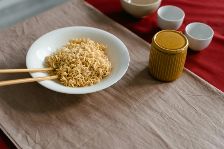 a bowl of noodles and chopsticks on a table, trending on unsplash, realism, on a velvet table cloth, yellow ochre, high quality product image”, made of glazed