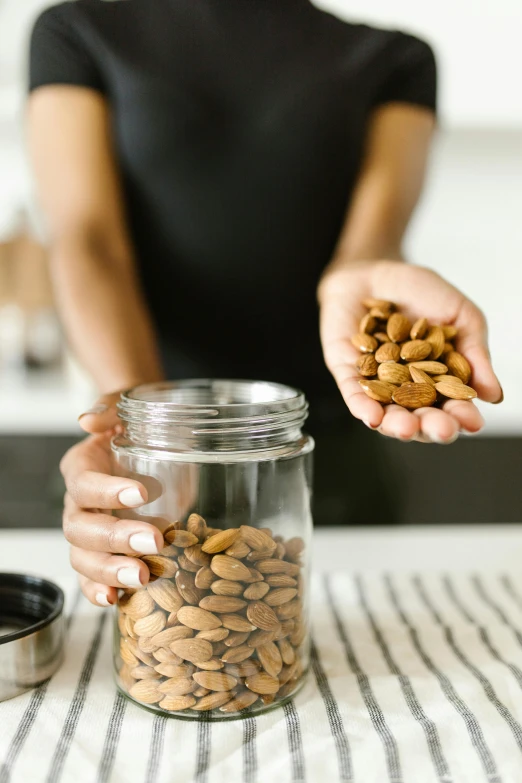 a woman holding a jar filled with almonds, hands on counter, curated collection, precision, brown