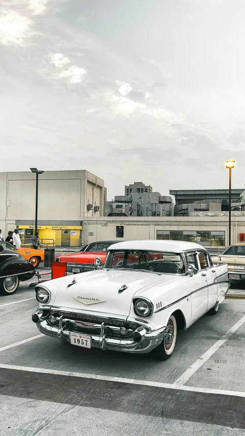 a white car is parked in a parking lot, a colorized photo, pexels contest winner, rooftop party, restomod, tehran, 1957 chevrolet bel air