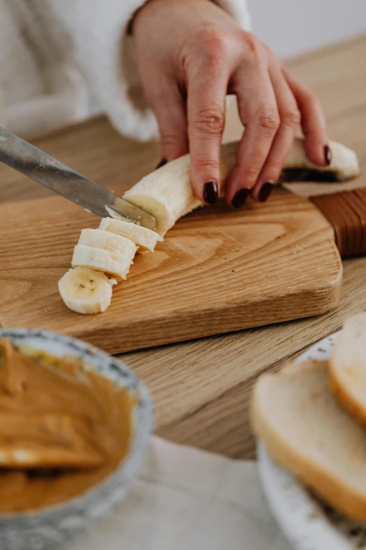 a person cutting a banana on a cutting board, inspired by Richmond Barthé, pexels contest winner, sandwich, natural wood top, vanilla, breakfast buffet