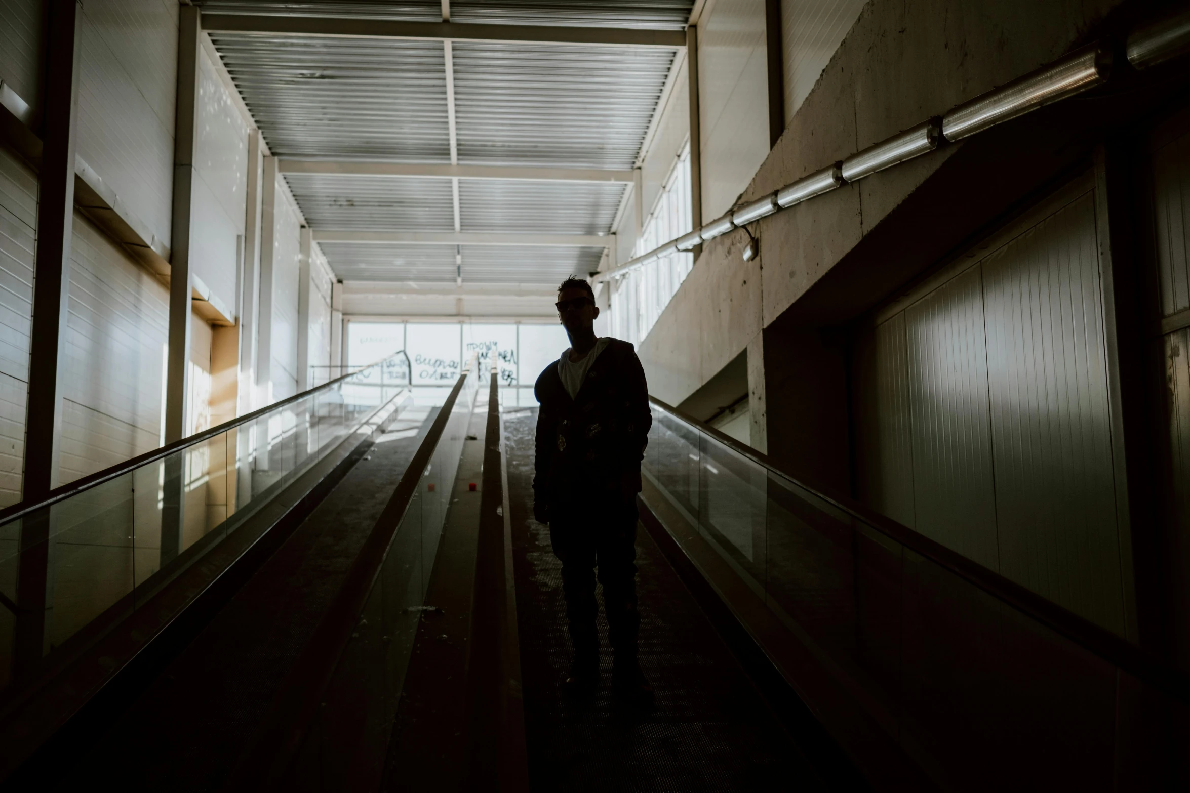 a person standing at the end of an escalator, an album cover, inspired by Elsa Bleda, realism, man in black, silhouette :7, high quality picture, an abandoned