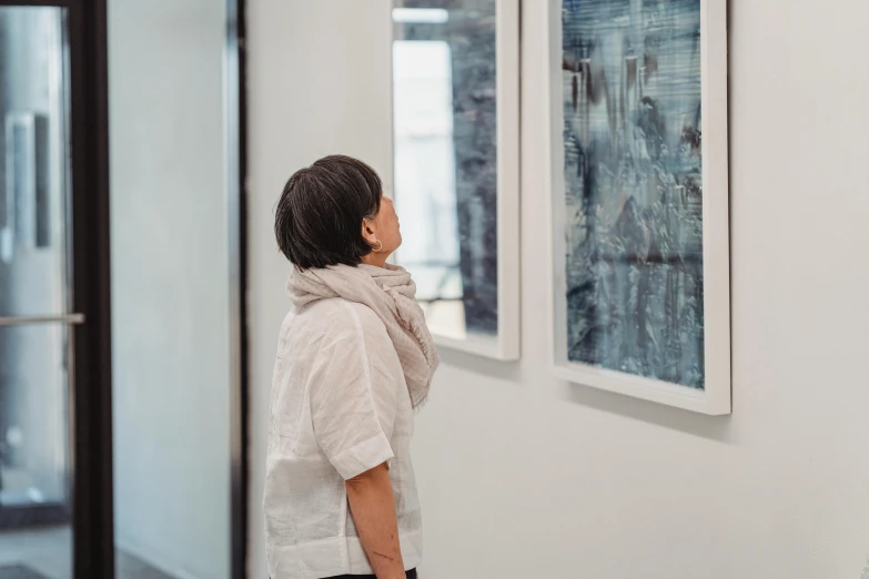 a woman looking at paintings on a wall, a hyperrealistic painting, by Matija Jama, pexels contest winner, cyanotype, fiona staples and kinu nishimura, side profile shot, looking outside