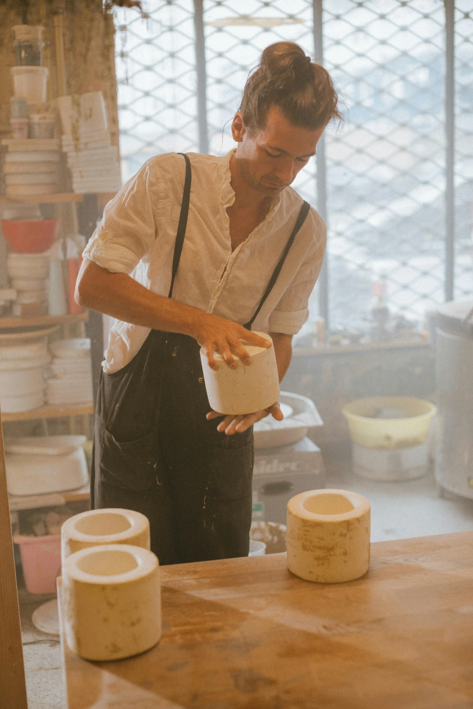 a man that is standing in front of a table, inspired by Hendrik Gerritsz Pot, trending on unsplash, large jars on shelves, white clay, production still, pouring