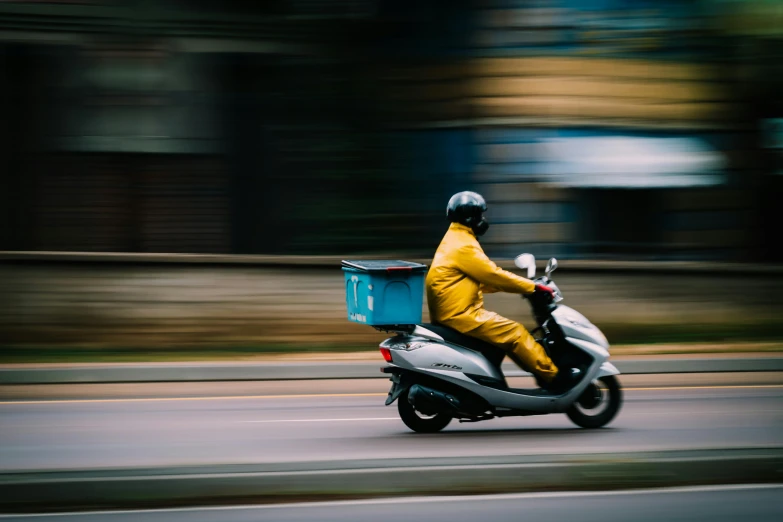 a man riding a motor scooter down a street, pexels contest winner, with yellow cloths, postage, panning shot, avatar image