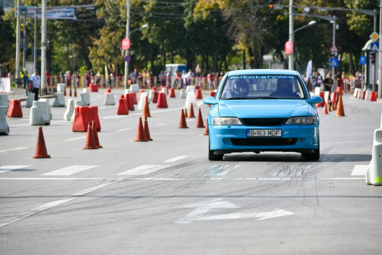 an electric blue car on a road surrounded by orange cone cones