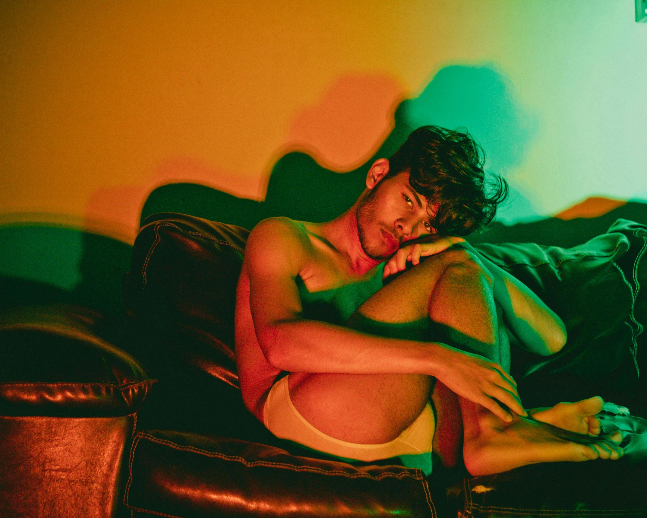 a man that is laying down on a couch, by Elsa Bleda, pexels contest winner, bisexual lighting, declan mckenna, red and green tones, tanned