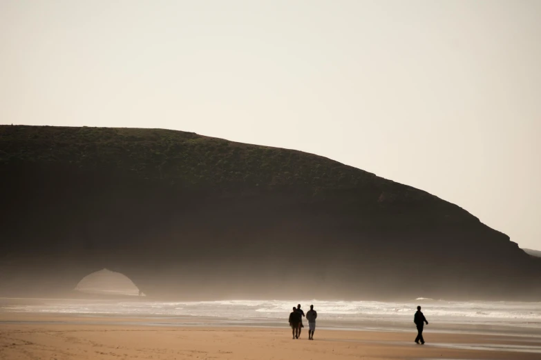 a group of people walking on top of a sandy beach, les nabis, moody hazy lighting, rock arches, marsden, profile image