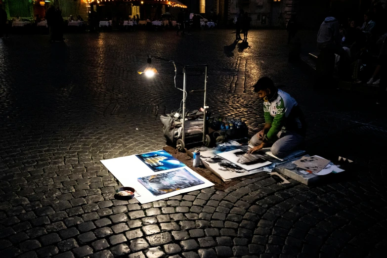 a man sitting on top of a cobblestone street, an airbrush painting, by Julia Pishtar, pexels contest winner, busy night, tending on art station, pantheon, art stand