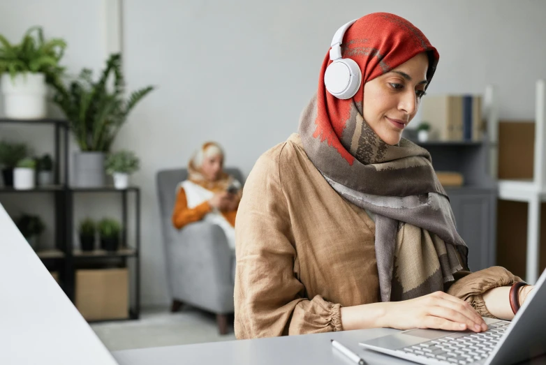 a woman sitting in front of a laptop wearing headphones, inspired by Maryam Hashemi, hurufiyya, middle eastern details, home office, covered in