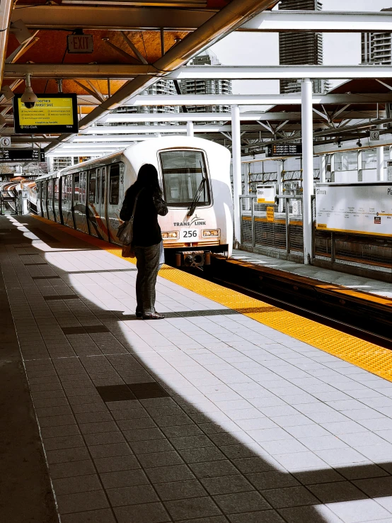 a woman waiting for a train at a train station, by Carey Morris, unsplash, hyperrealism, vancouver, orange line, white panels, olympus platform