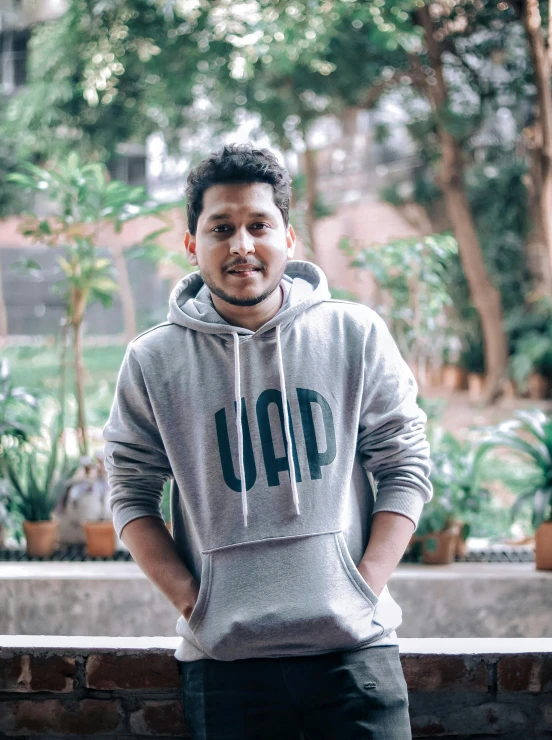 a man in a grey sweatshirt is standing in front of a brick wall