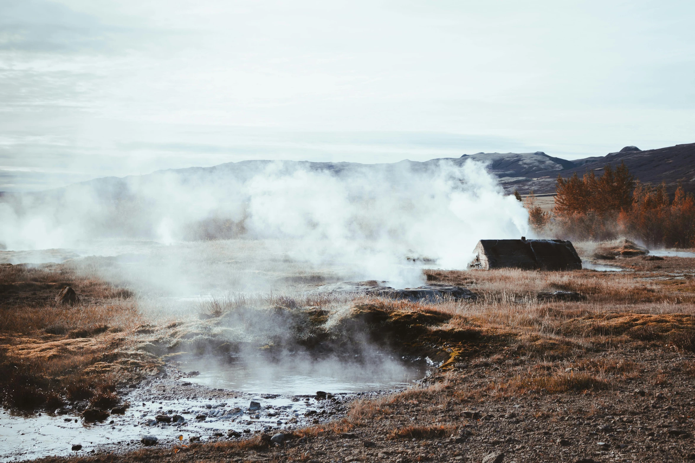 steam rises from the ground next to an old house