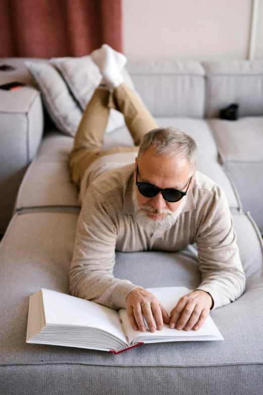 a man laying on a couch reading a book, implanted sunglasses, dark grey haired man, 2019 trending photo, architect