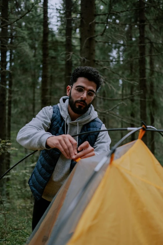 a man standing next to a tent in the woods, a portrait of rahul kohli, eng kilian, adventure gear, profile image