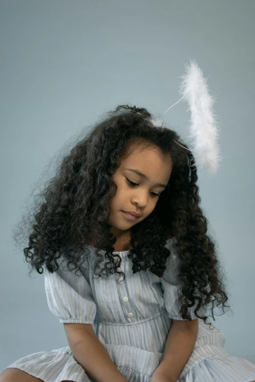 a little girl sitting on the ground with a feather in her hair, an album cover, inspired by Theo Constanté, pexels contest winner, renaissance, mixed race, an angel standing still, close - up studio photo, holiday