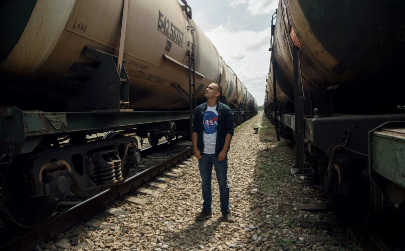 a man standing in front of two train cars, inspired by Alan Bean, unsplash, propane tanks, film still of barack obama, dasha taran, spacex