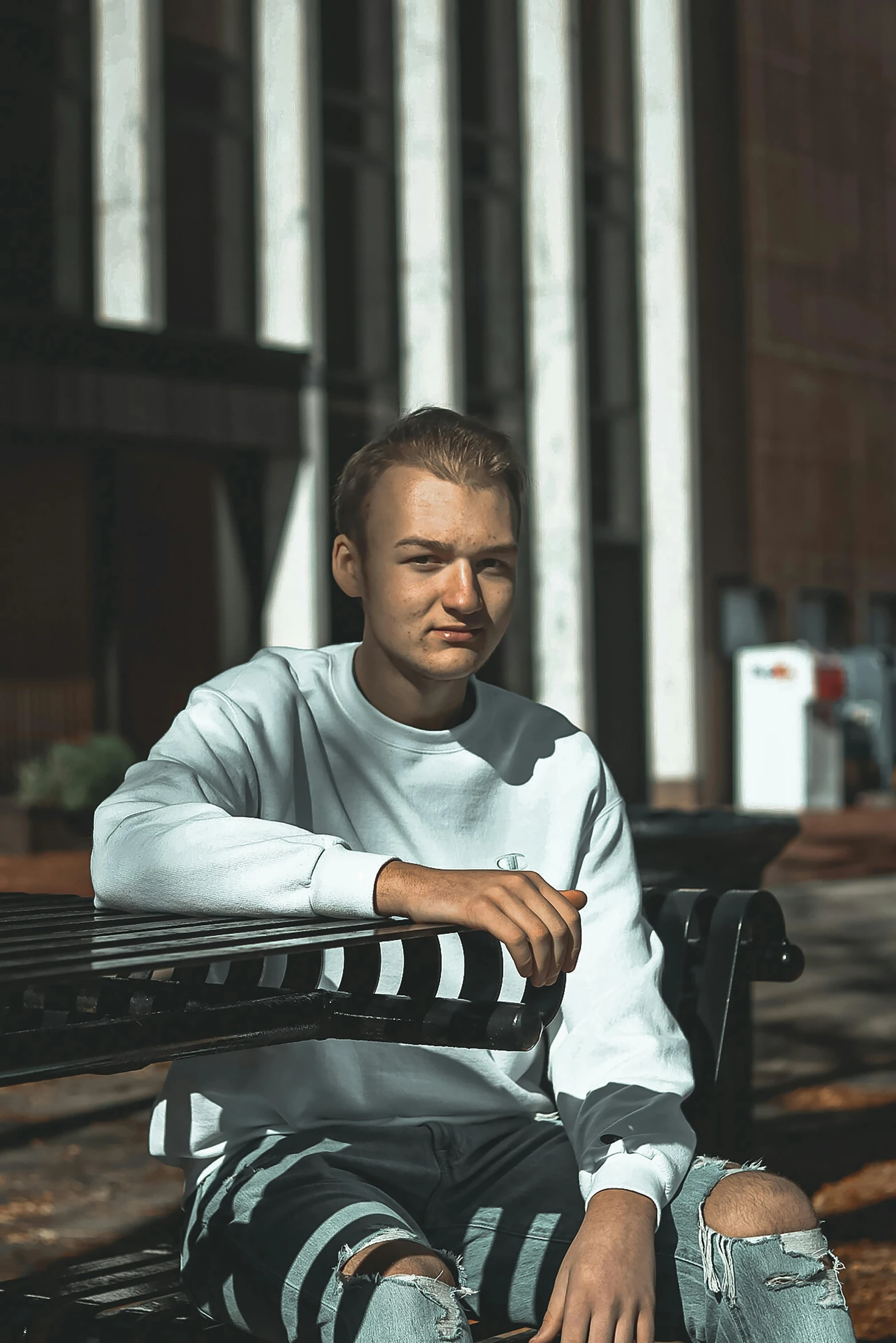 young man sitting on park bench wearing striped pants