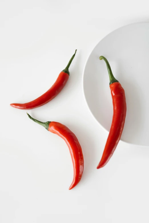 three chili peppers sitting on top of a white plate, a picture, trending on pexels, detailed product image, smooth curves, tall thin, lulu chen