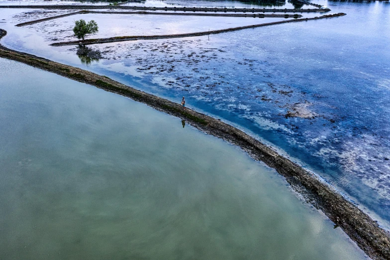 a large body of water next to a forest, a picture, inspired by Steve McCurry, unsplash contest winner, hurufiyya, malaysia with a paddy field, flooded fishing village, lone person in the distance, blue waters