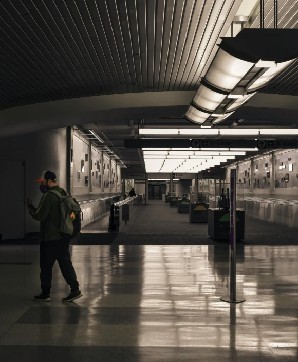 a man standing in the middle of a train station, by Carey Morris, unsplash contest winner, lowkey lighting, non-binary, obscured hooded person walking, reflective floor