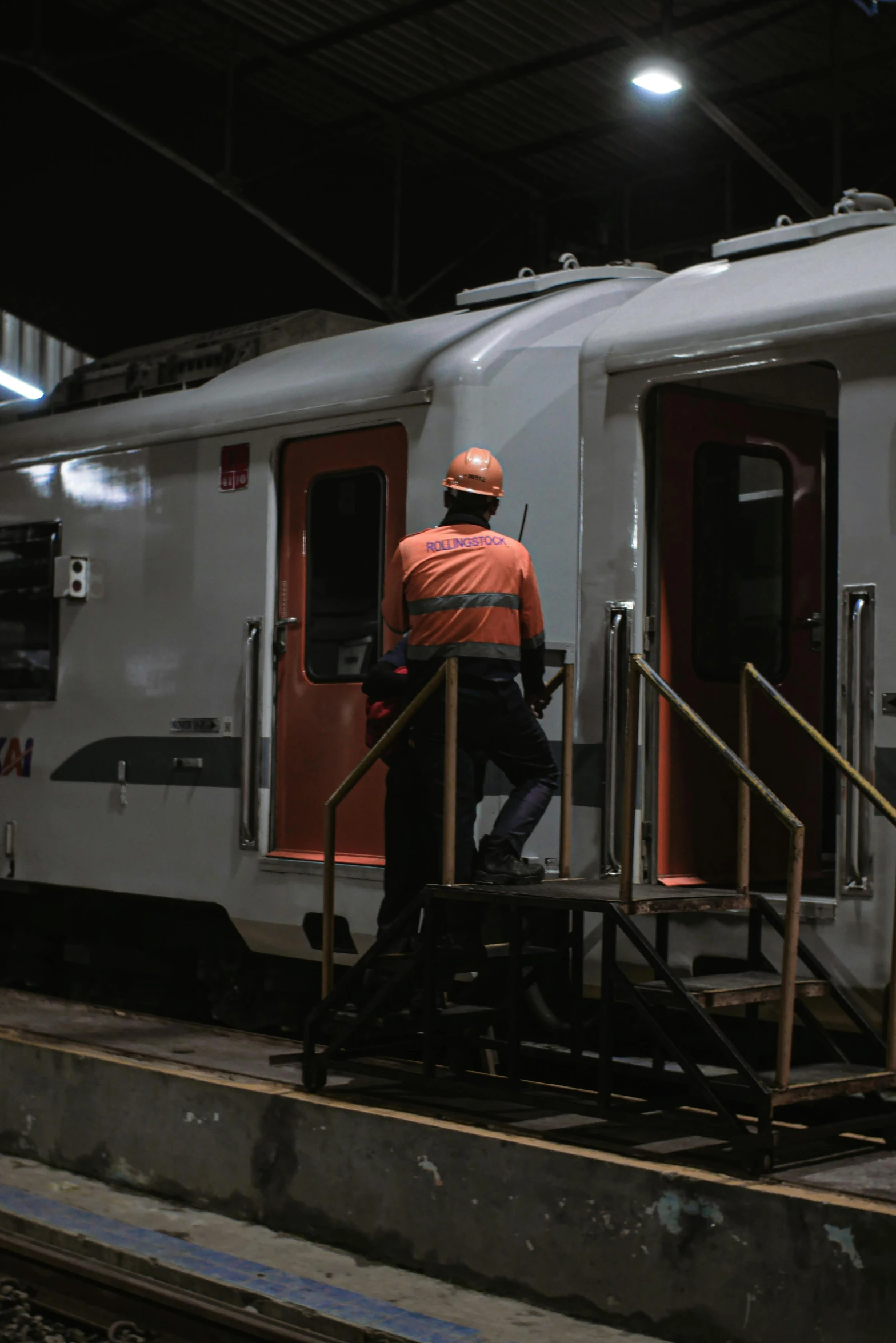 a man that is standing in the doorway of a train, orange and white, maintenance area, busy night, thumbnail