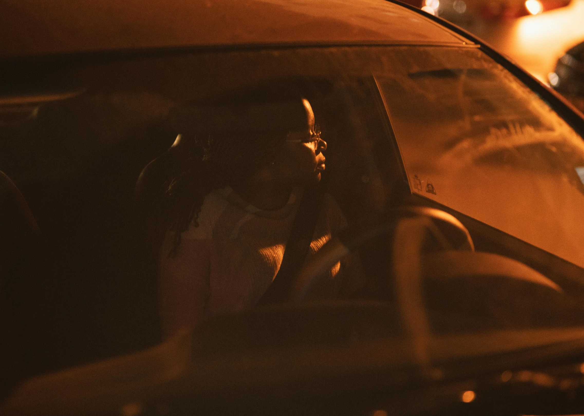 a woman sitting in the driver's seat of a car, by Dan Frazier, pexels contest winner, dark-skinned, ambient amber light, reflecting, low quality footage