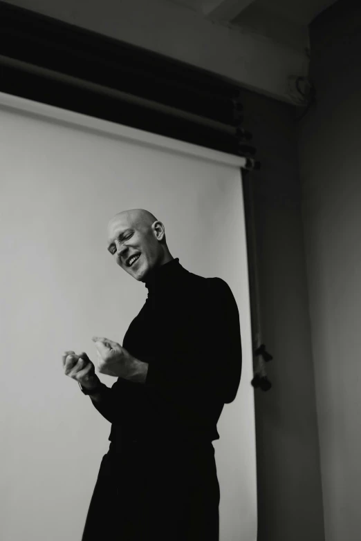 a man standing in front of a projector screen, a black and white photo, unsplash, hyperrealism, bald head, laughing, jean paul gaultier, norman foster