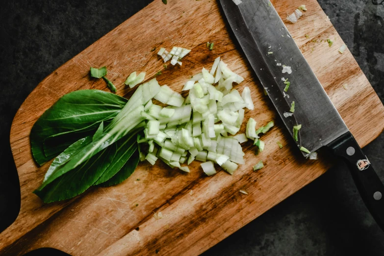 a knife sitting on top of a wooden cutting board, unsplash, light greens and whites, celery man, onions, basil gogos