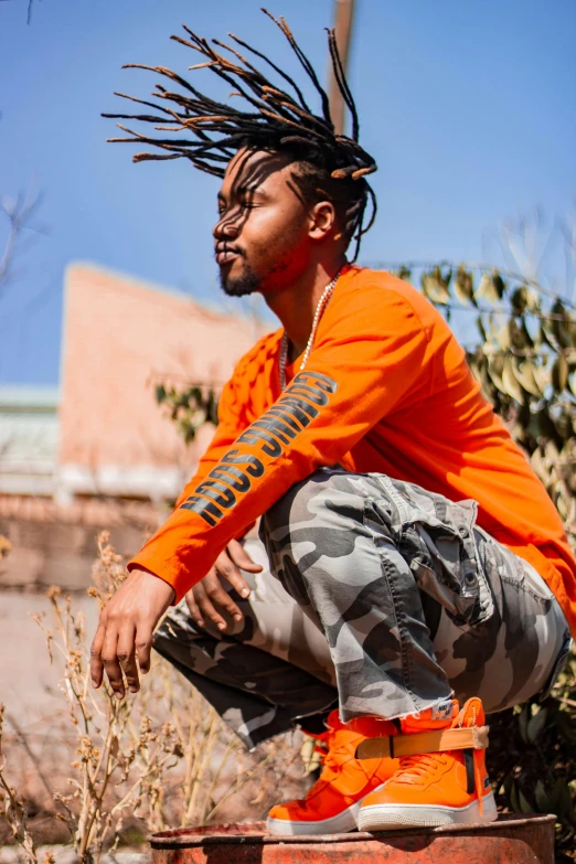 a man with dreadlocks sitting on a fire hydrant, trending on unsplash, wearing orange prison jumpsuit, bright sunny day, techwear look and clothes, profile image