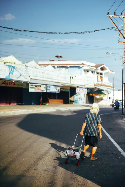 a man riding a skateboard down the middle of a street, by Andrew Stevovich, aruba, market stalls, 1990s photograph, elderly